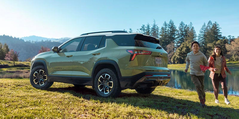 Two kids running behind a parked 2025 Chevy Equinox by lake